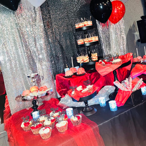 A dessert table with red and black decor, featuring cupcakes, cake pops, and parfaits.
