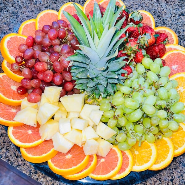A vibrant fruit platter with pineapple, red and green grapes, strawberries, and grapefruit slices.