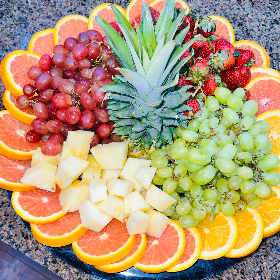 A vibrant fruit platter with pineapple, red and green grapes, strawberries, and grapefruit slices.