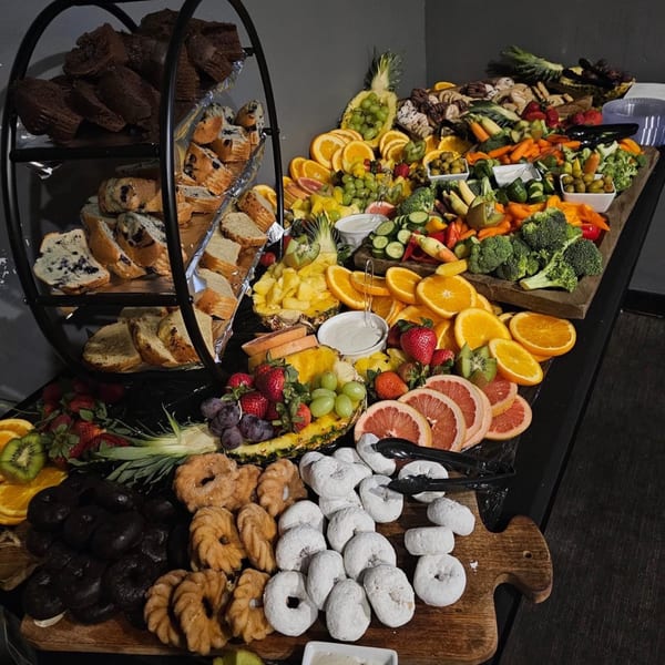 A large buffet spread with pastries, fresh fruit, and vegetables with dip on a dark table.
