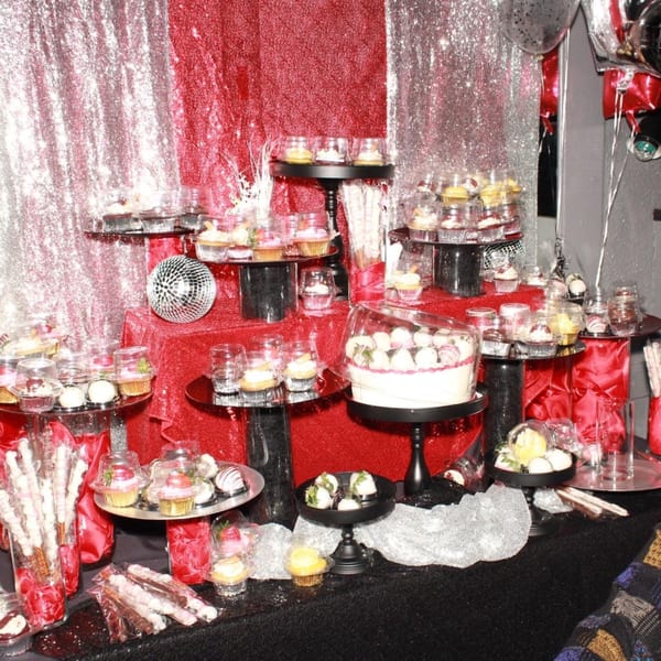 A dessert table with cupcakes, chocolate-covered strawberries, and other treats on red and silver sequined fabric.