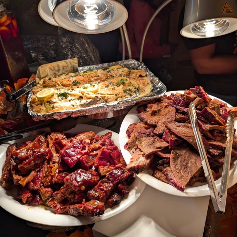 Buffet spread with baked fish, BBQ ribs, and sliced brisket under heat lamps.