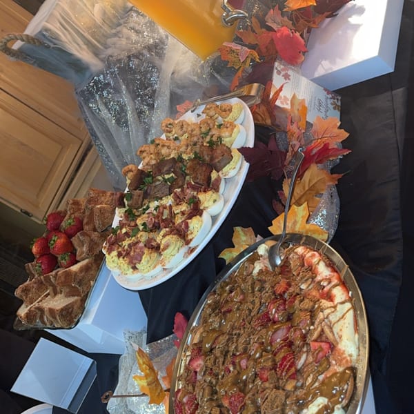 A buffet spread featuring deviled eggs, shrimp, sliced bread, strawberries, and a dessert pizza.