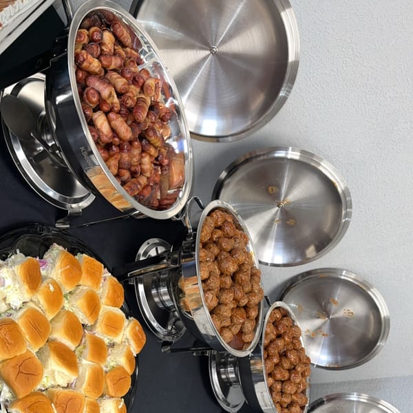 Chafing dishes filled with bacon-wrapped sausages and meatballs, alongside a platter of slider buns.