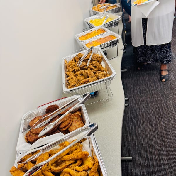 A buffet line with trays of fried chicken, mac and cheese, baked beans, and other fried foods.