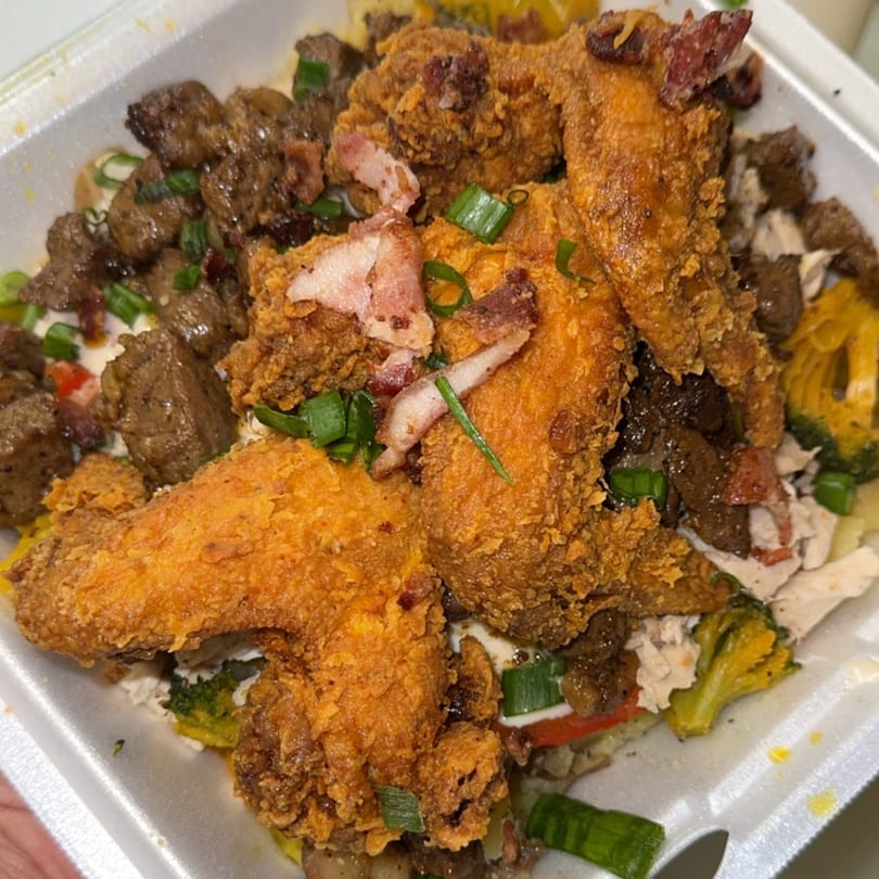Crispy fried chicken wings, steak, and vegetables in a takeout container.