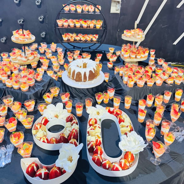 A dessert table with a bundt cake, fruit parfaits, and strawberries in "60" shaped dishes.